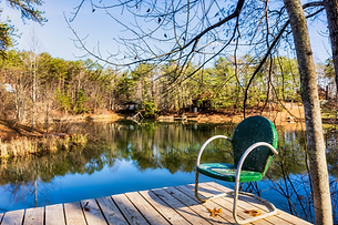A metal green chair on a dock over a pond on a sunny day in the Smoky Mountains.