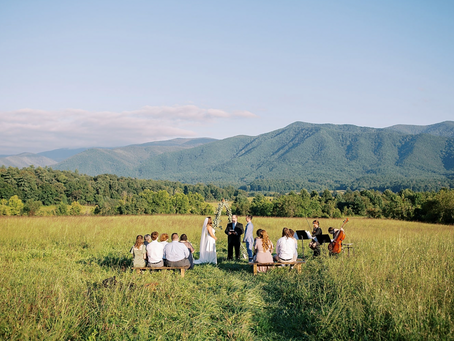 A couple exchanging their vows in front of a minister and guests with the Smoky Mountains in the background