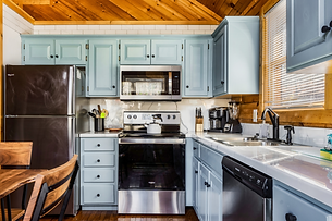 Light blue painted kitchen cabinets with marble countertops and stainless steel appliances in a cabin.