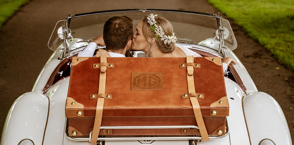 Brudepar kysser i en hvid bil med en brun kuffert, Dan Mortensen Foto