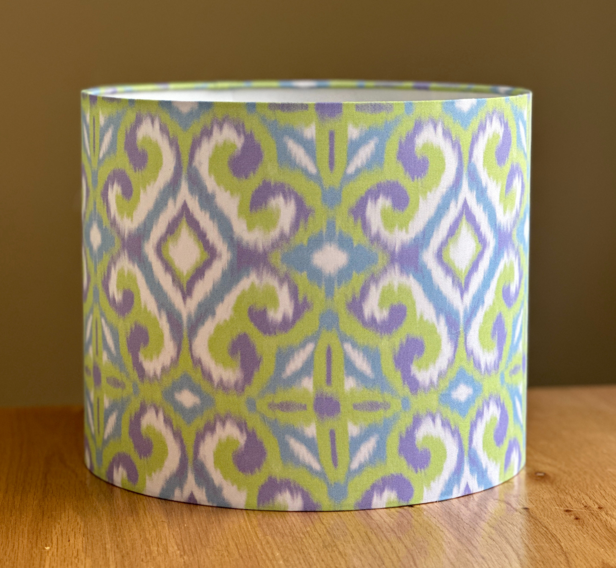 Cylindrical lampshade with pastel ikat diamond pattern in soft green, lavender, white, and sky blue on fabric.
