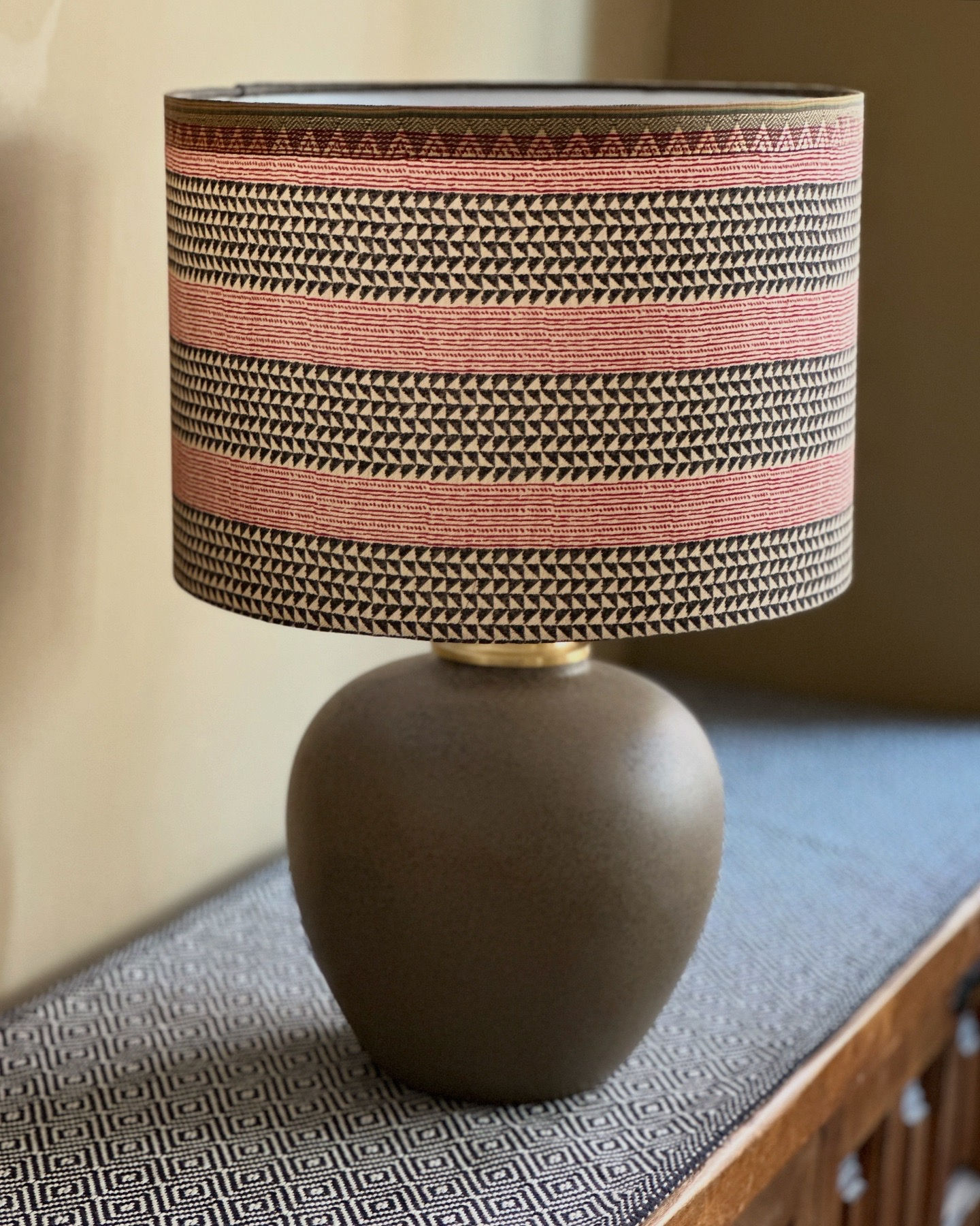 Handmade table lamp with ethnic brown and red lampshade on a taupe ceramic base.