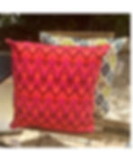 Handmade cushion with vibrant ikat pattern in red, orange, and magenta, named Wild Paprika in a natural garden enviroment.