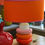 Thumbnail: Bold table lamp with orange, pink, and red ceramic base and a bright orange lampshade with pink trim.