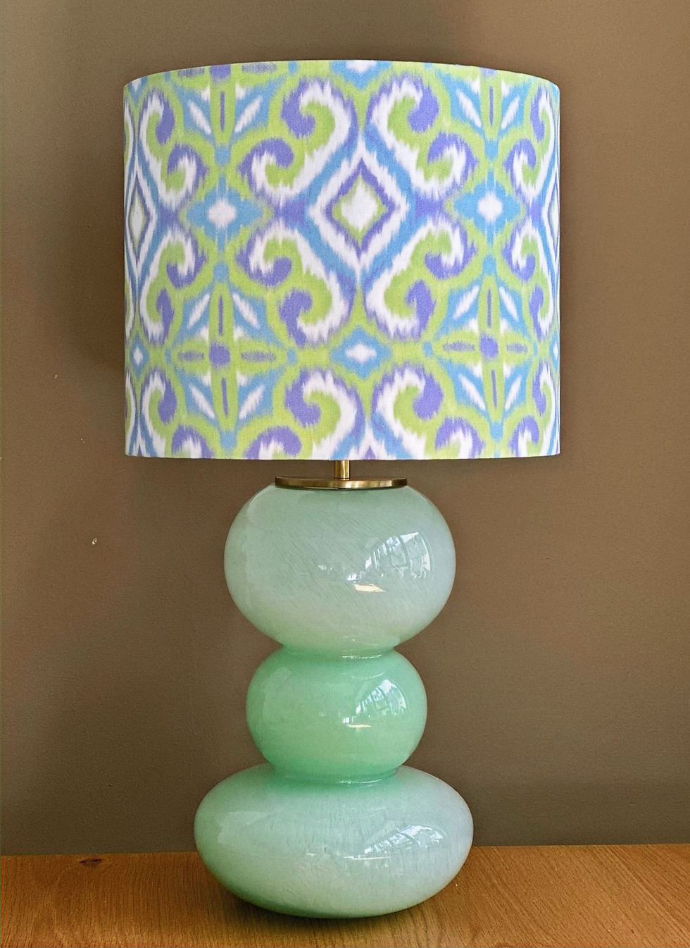 Thumbnail: Mint green glass lamp base with rounded stacked shapes, with a colorful ikat fabric lampshade in lilac, lime and sky blue