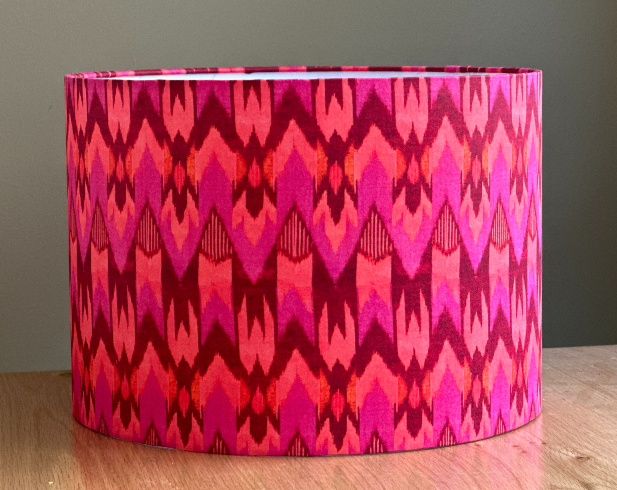 Cylindrical lampshade with bold ikat pattern in vibrant shades of hot pink, fuchsia, and red on fabric