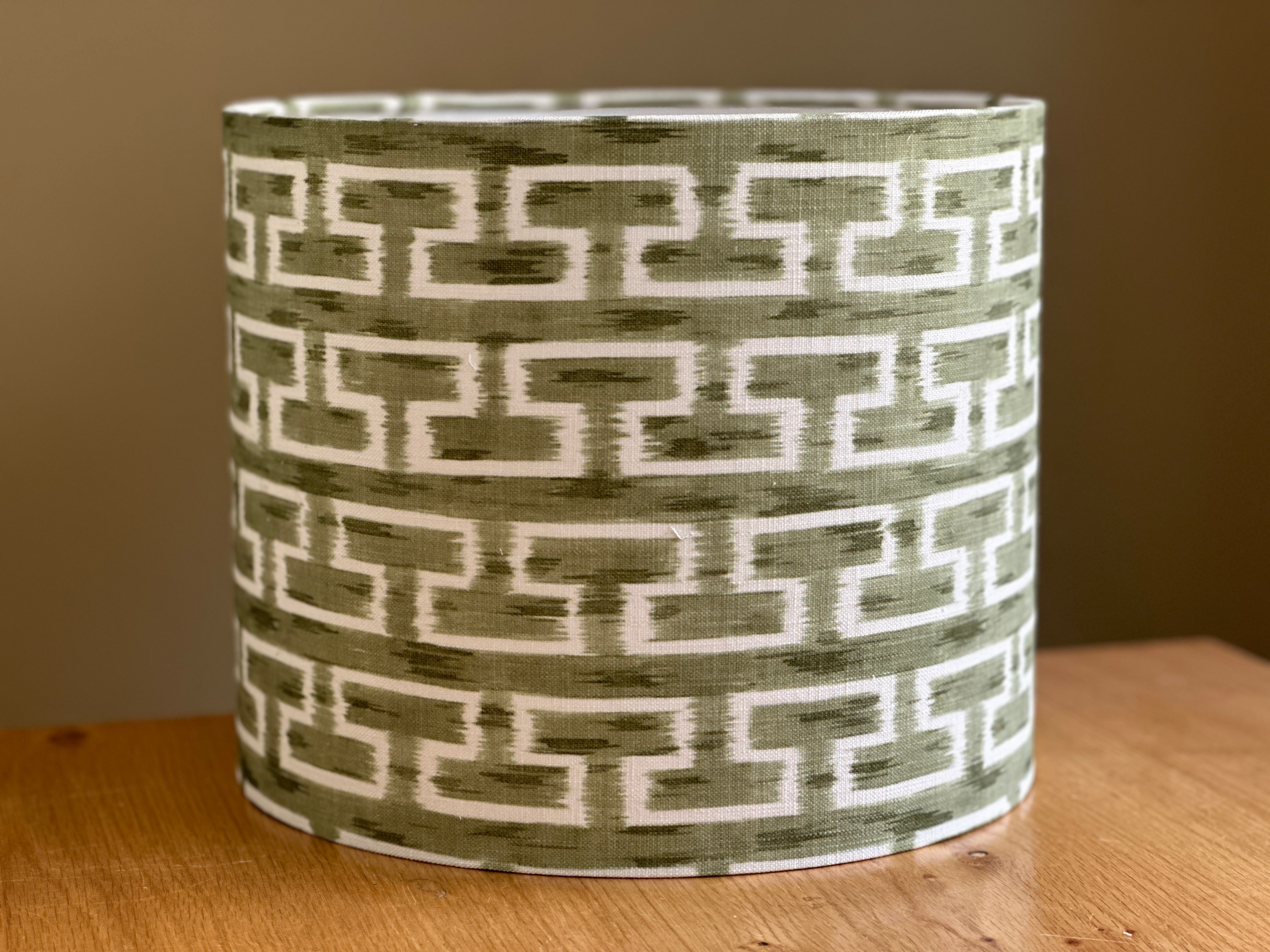 Cylindrical lampshade with an olive green and white geometric ikat pattern on natural textured fabric