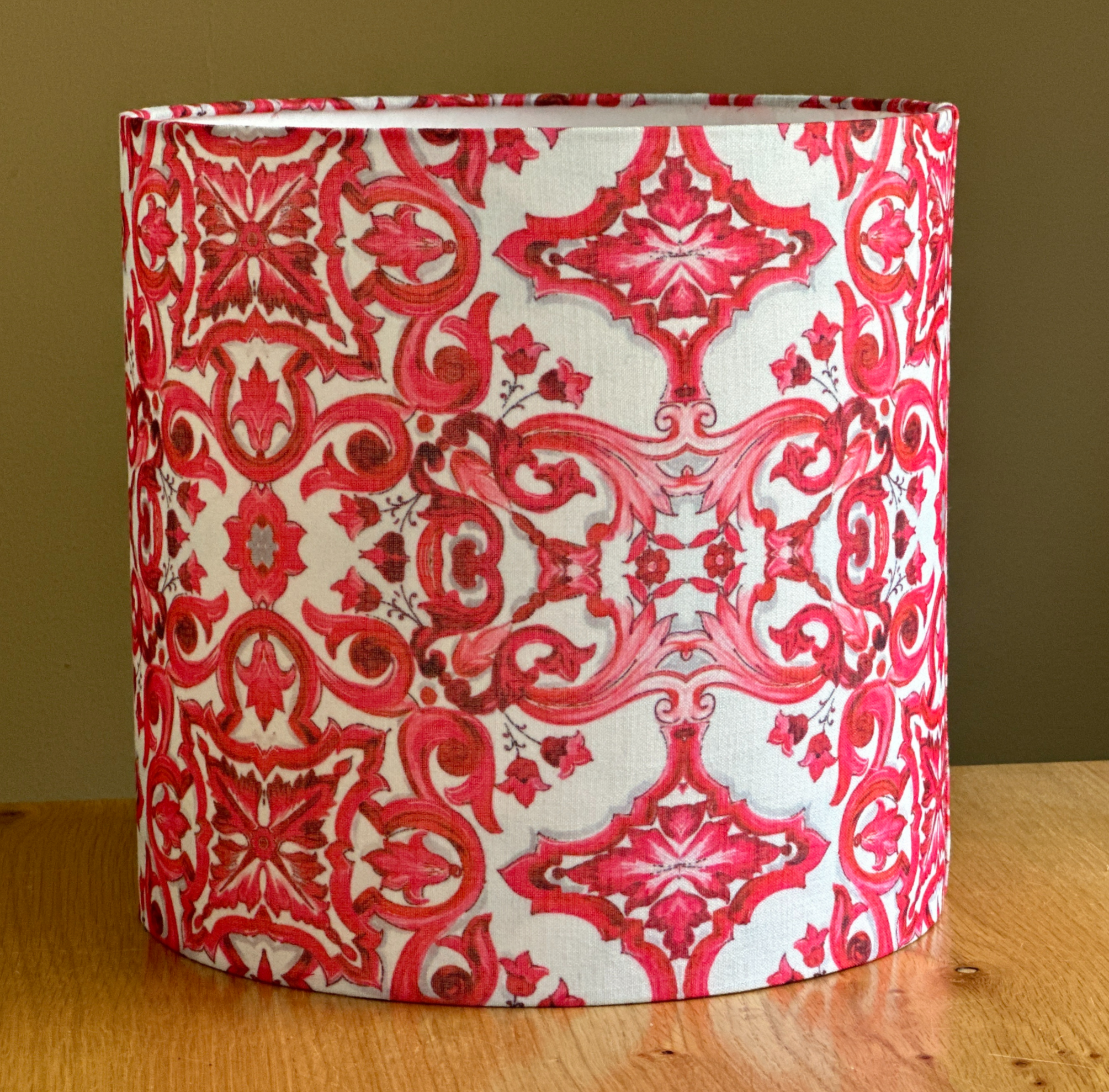 Cylindrical lampshade with red ornamental motifs on white fabric, featuring a symmetrical, Moroccan-style pattern.