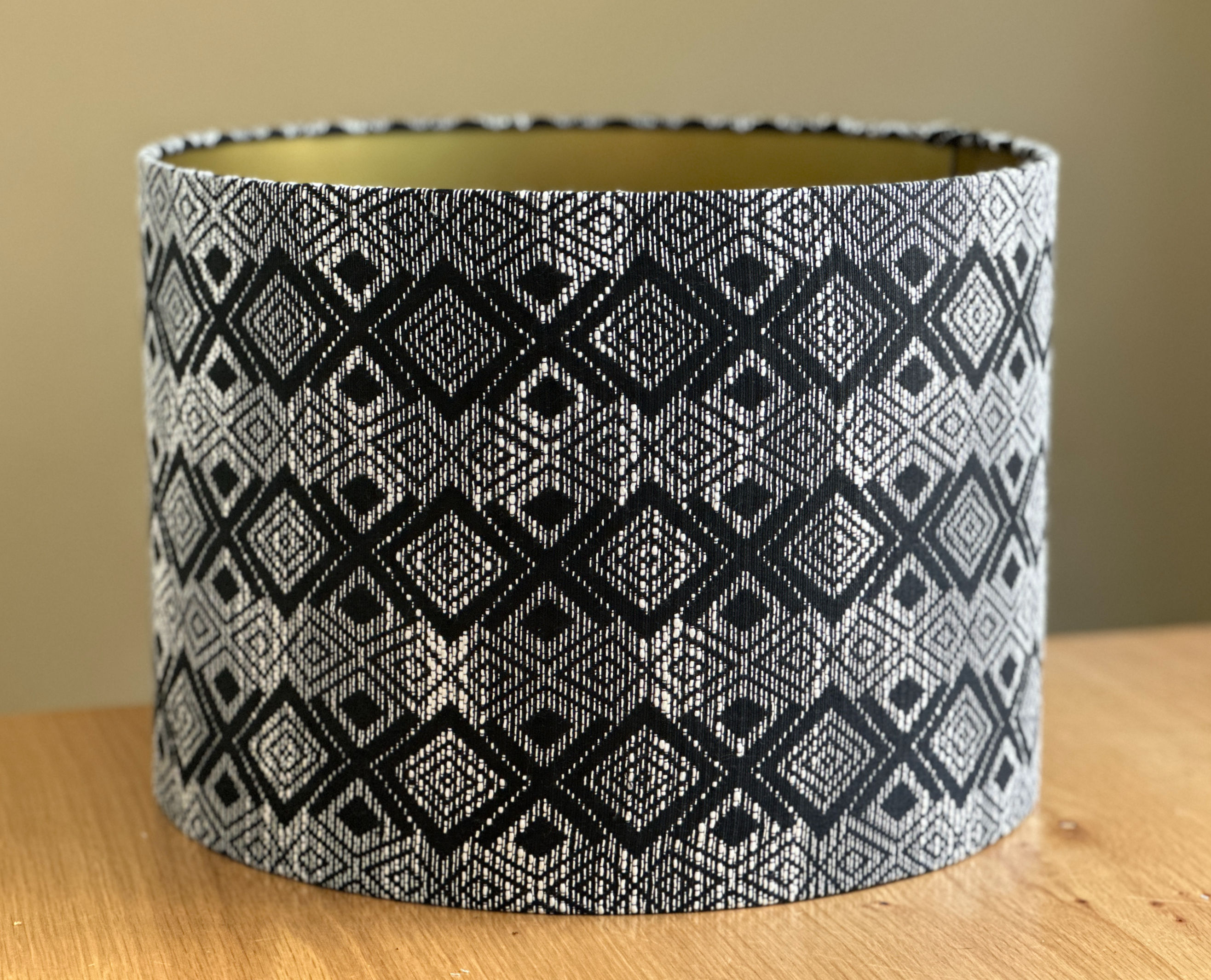 Cylindrical lampshade with black and white geometric diamond pattern inspired by Afrikaans tribal textiles, featuring a gold