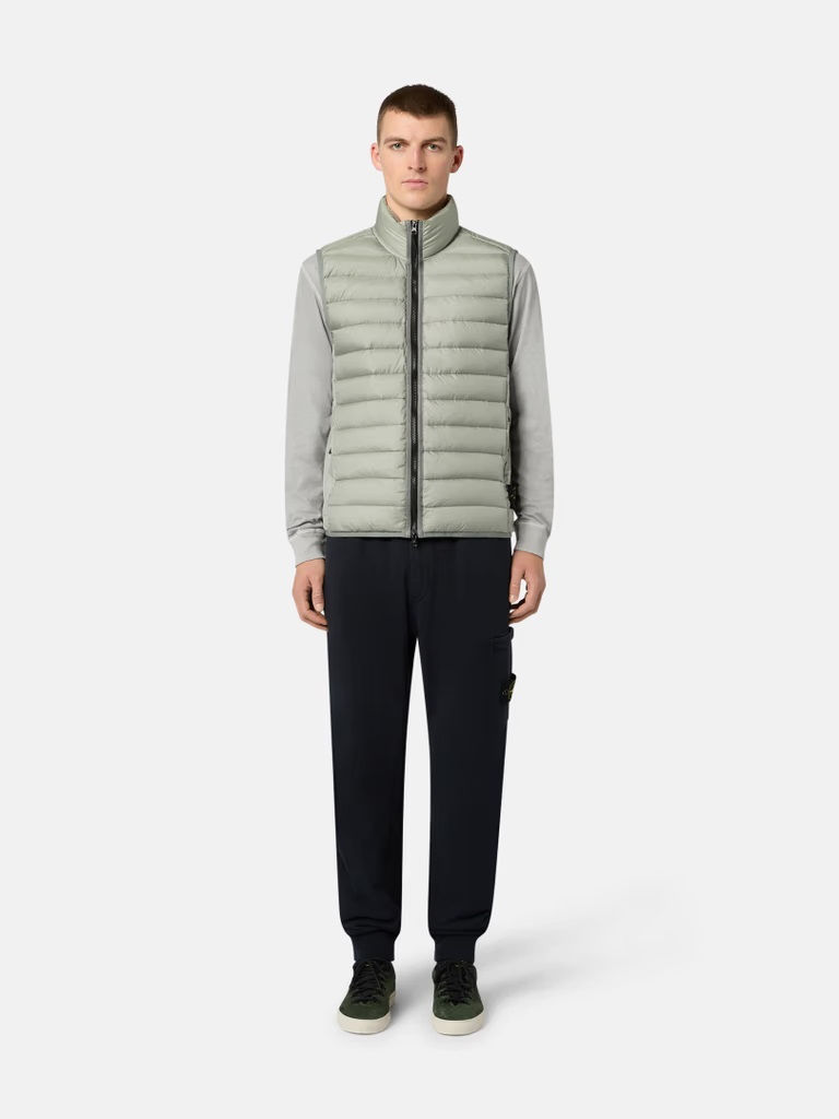 Homme portant un gilet matelassé vert clair, pantalon noir.  Boutique Karsenty