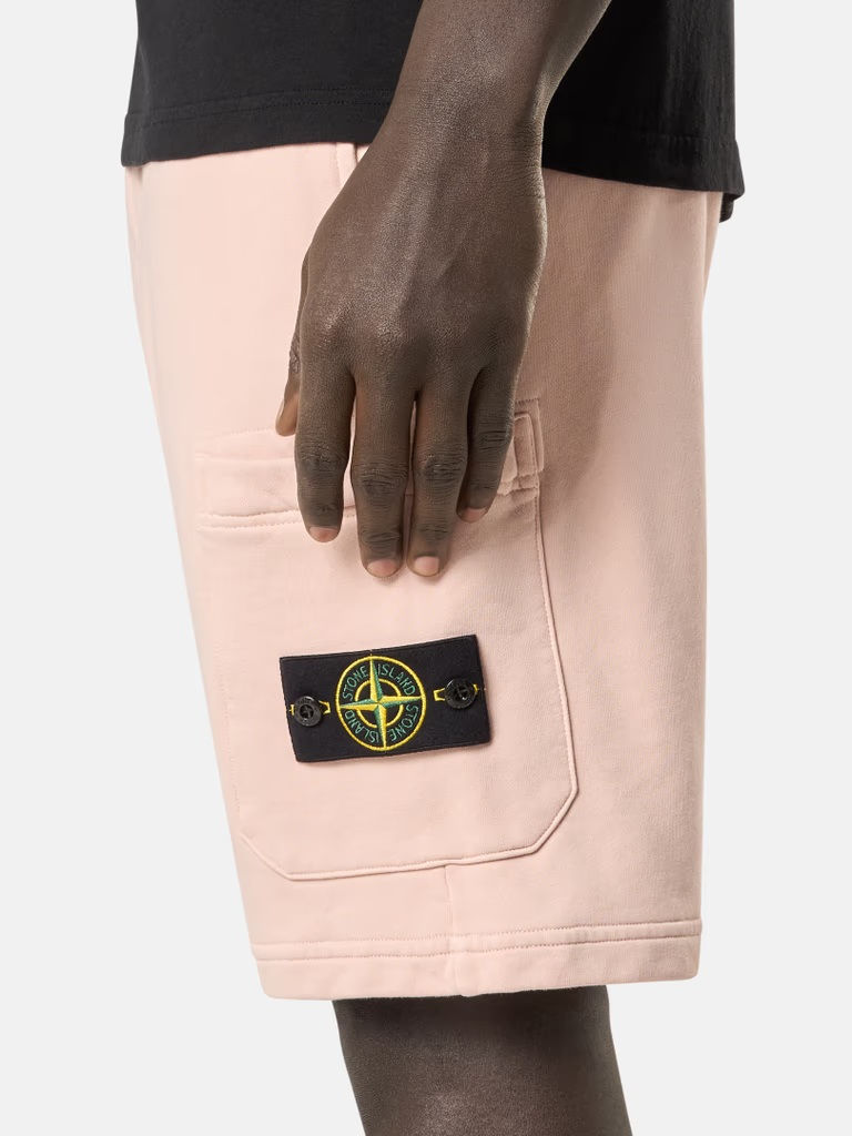 Miniature : Homme portant un short rose avec un patch vert et noir, détail vestimentaire.