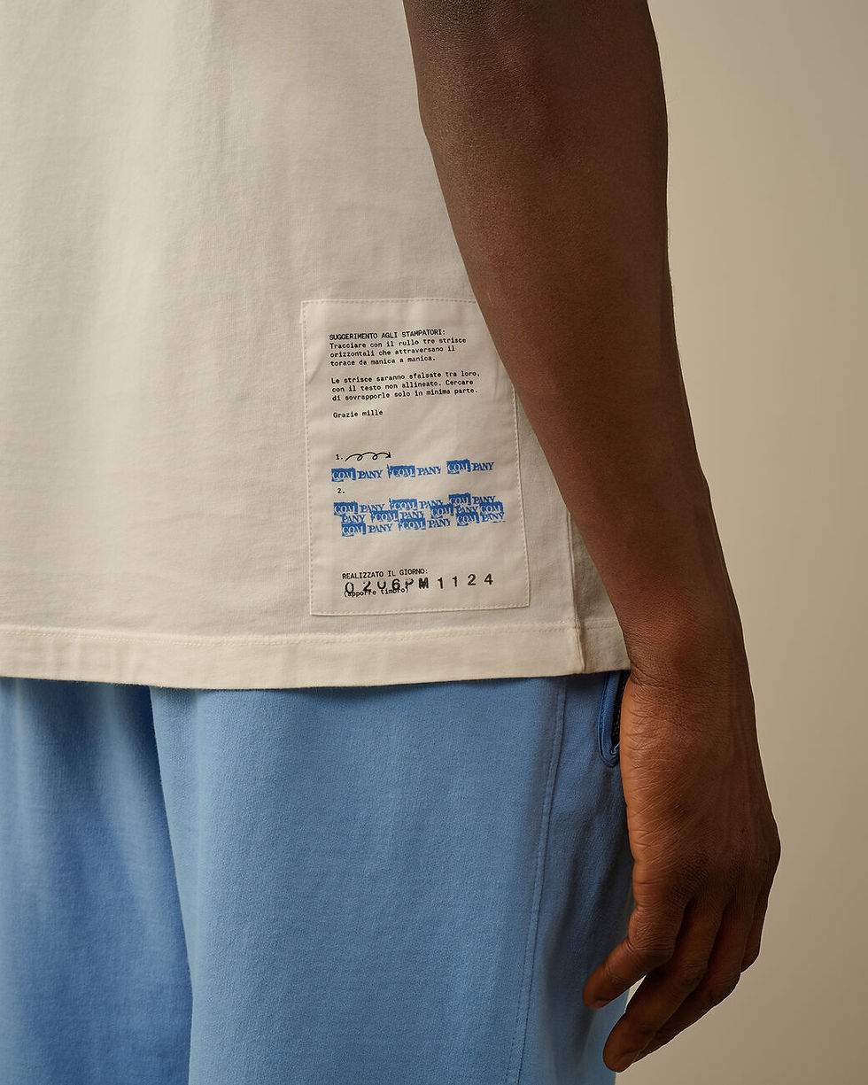 Miniature : Gros plan d'un t-shirt beige avec des étiquettes bleues et Boutique Karsenty.