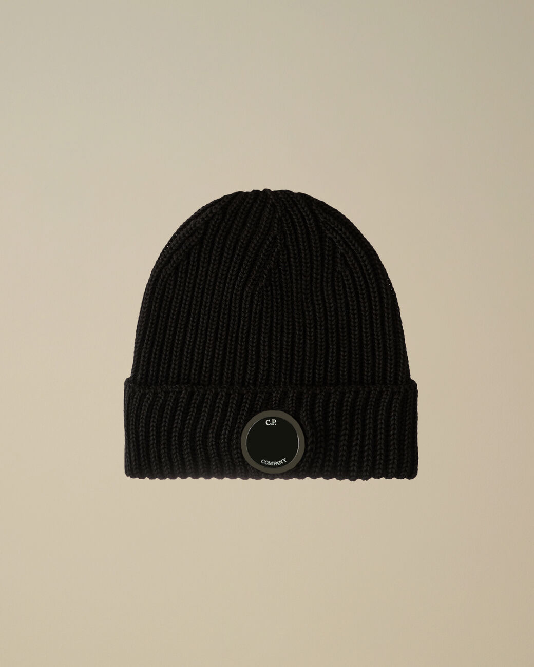 Un bonnet noir tricoté, avec logo circulaire, sur fond beige clair.