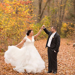 A bride and groom dance in the orange and yellow fall leaves in front of a forest background.