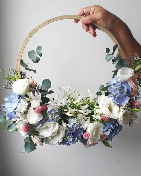 A hoop bouquet with a light wood handle and white, blue, and pink flowers.