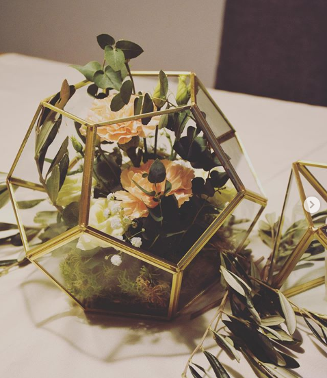 A small arrangement of flowers on a white table with a hexagonal cage of gold around them.