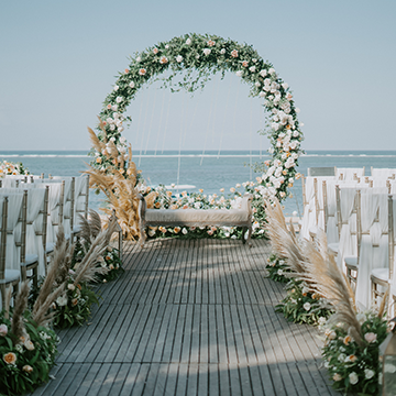 A circular arch sits in front of a port with white chairs and large tufts of pampas grass lining the walkway.