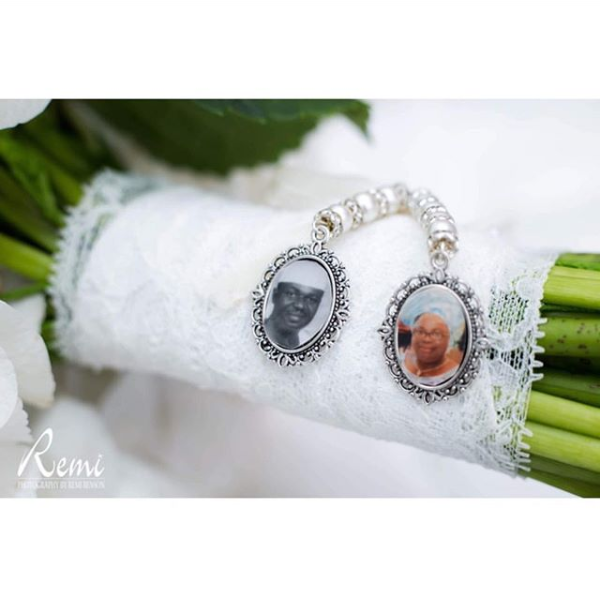 A green bouquet handle wrapped in white lace with two silver charms holding pictures of loved ones passed.