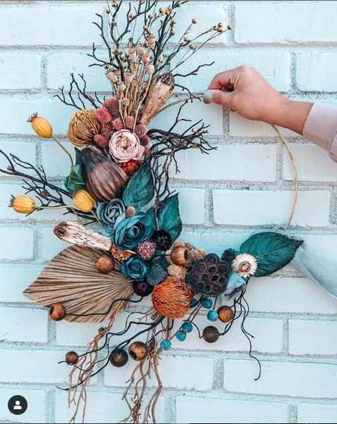A hoop bouquet with teal, nontraditional flowers such as seed pods and large leaves.