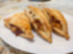 Three golden-brown apple turnovers with flaky crusts sit on a white plate, placed on a marbled countertop. Filling is visible inside.