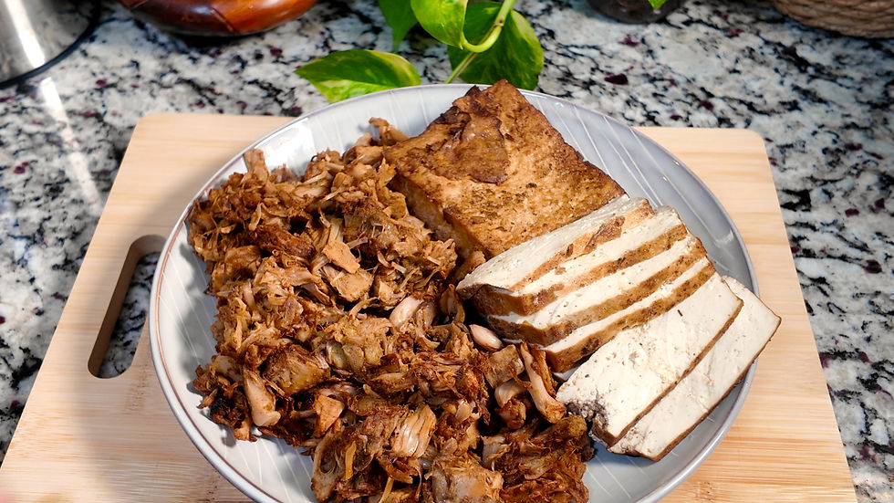 Plate of roasted jackfruit and sliced tofu on a wooden board, granite countertop in the background, with green plant leaves adding a fresh touch.