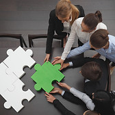 Group of business people assembling final piece of jigsaw puzzle, team work support unity