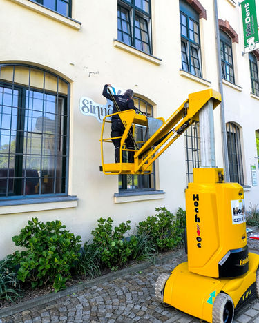 Person on yellow lift restoring "Sanpje" lettering, advertising technology Chemnitz.