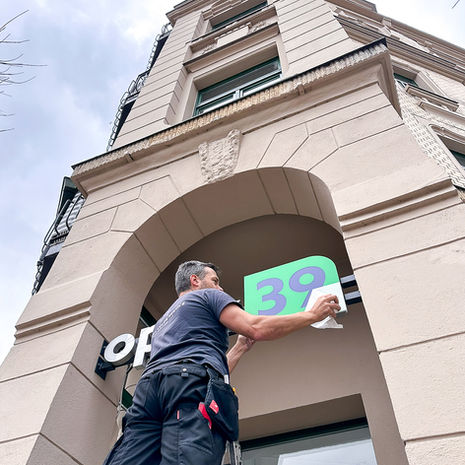 Mann installiert grünes Schild "39" an Gebäudefassade, werbetechnik chemnitz kosten.