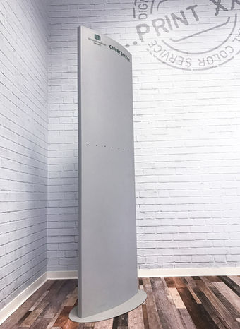 Slim grey display stand with "PRINT" on brick wall, advertising technology Chemnitz costs.
