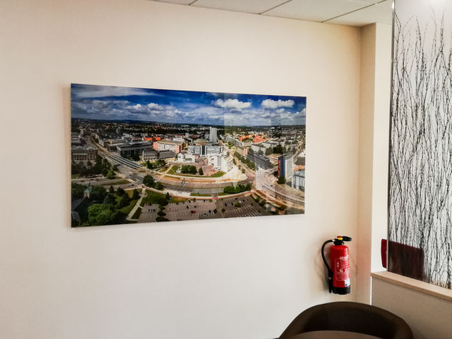 Großformatiges Luftbild einer Stadtansicht an weißer Bürowand montiert. Modernes Wandbild, sich wiederholende Betonstruktur unter blauem Himmel dargestellt. UV Direktdruck auf Aludibond mit verdeckter Wandmontage Chemnitz