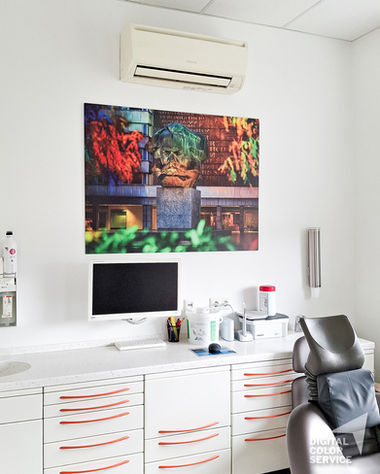 Modernes Zahnarztzimmer mit Behandlungsstuhl, bunten Wandbildern, weißen Schränken und Klimaanlage. UV Direktdruck auf Aludibond mit verdeckter Wandmontage