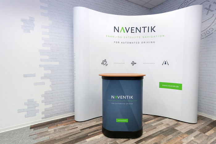 Naventik exhibition stand with counter, text “ENABLING SATELLITE NAVIGATION” and “Contact us”.