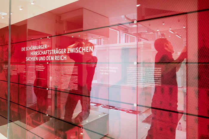 Moderne Ausstellung mit Text "Schönburger-Herrschaftsträger zwischen Sachsen und Reich" und roten Reflexionen. Wir haben großflächig die Digitaldruckfolien verklebt.