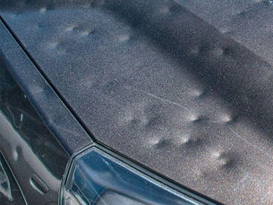 Capô de carro preto com várias amassadas, vista do farol dianteiro, refletindo luz intensa.
