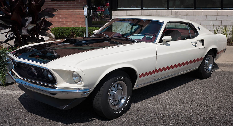 Carro clássico Mustang Mach 1 branco e preto estacionado na rua, com capô preto e texto 351; clima ensolarado.