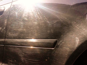 Close-up da lateral de um carro preto com muitos riscos, refletindo forte luz do sol.