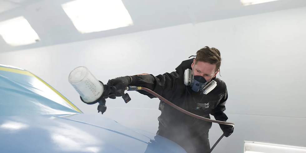 Homem de máscara pulveriza peelclear em um carro azul em cabine de pintura branca, com foco e névoa no ar.