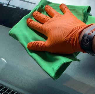 Pessoa passando uma microfibra limpa sobre o vidro do carro, removendo sujeira e deixando a superfície transparente.