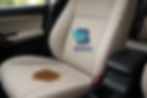 Banco de carro de cor clara com grande mancha de café, destacando o tecido sujo e necessidade de limpeza profissional.