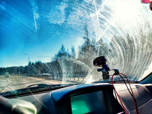 Vista interna de um carro mostrando o para-brisa com muita sujeira e oleosidade, prejudicando a visibilidade e criando um aspecto embaçado.