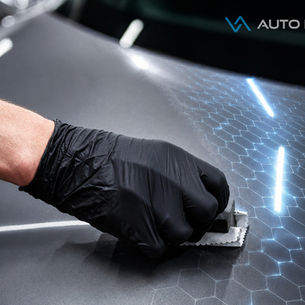 Mão com luva preta aplica proteção coating cerâmico (vitrificador) em capô de carro cinza com padrão hexagonal representando proteção criada pela camada; logo AUTO LEDS no canto superior.