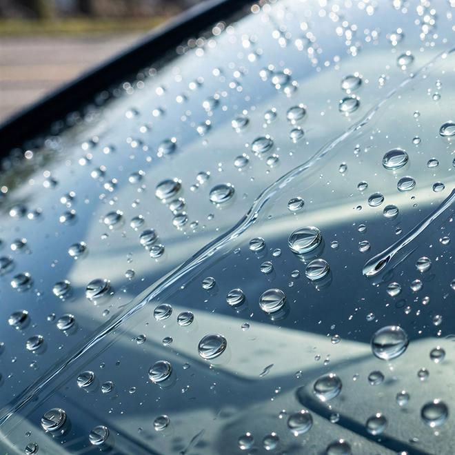 Close-up de gotas de chuva no para-brisa de um carro, com reflexos suaves e brilho azulado.