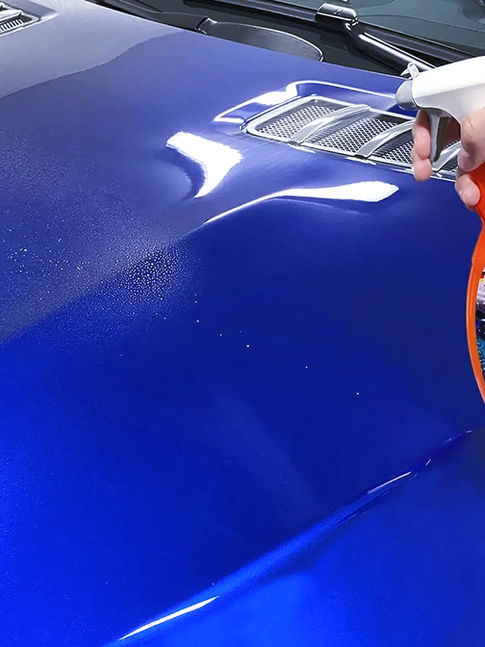 Mão pulveriza revestimento selante cerâmico SONAX no capô azul de carro, com brilho refletido e dutos de ar.