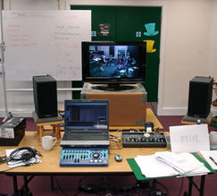 Studio control room with monitors, mixing desk, and laptop