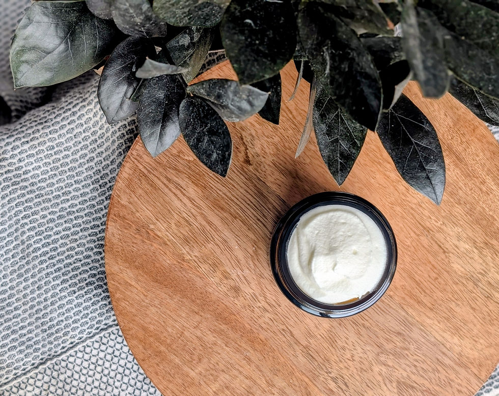 Looking down in an amber glass jar filled with white whipped butter sitting on a wooden table with a plant on a woven towel