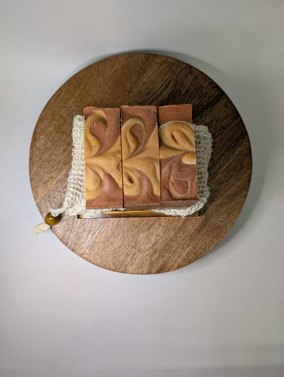Thumbnail: looking down on three bar soaps in a row sitting on a soap back on top of a circle piece of wood
