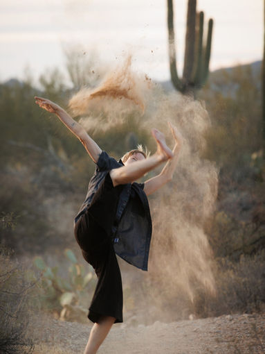 Haas with one foot on the ground and the other raised above head in a cloud of dust in the Tucson desert