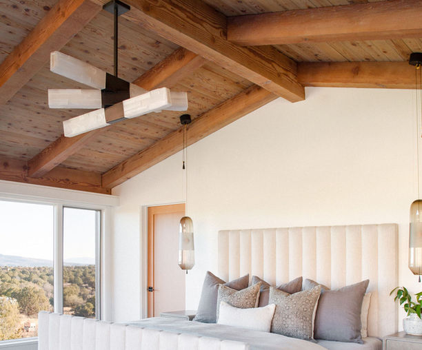 Lucca selenite chandelier installed in a luxury bedroom, featuring illuminated natural selenite crystal bars arranged in a sculptural geometric composition. Suspended beneath a vaulted wood-beam ceiling, the handcrafted fixture serves as an architectural focal point while providing warm ambient illumination.