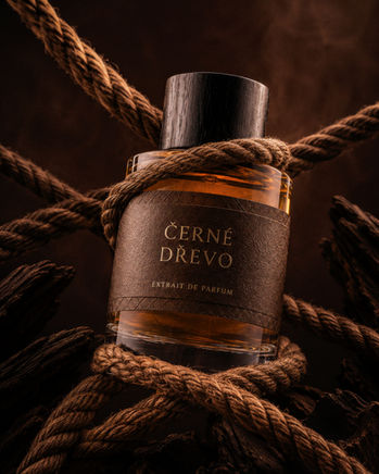 Černé Dřevo oud perfume bottle in a dark amber luxury campaign scene.