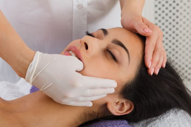 A therapist wearing gloves works inside the mouth of a client who suffers from TMJ Disorder